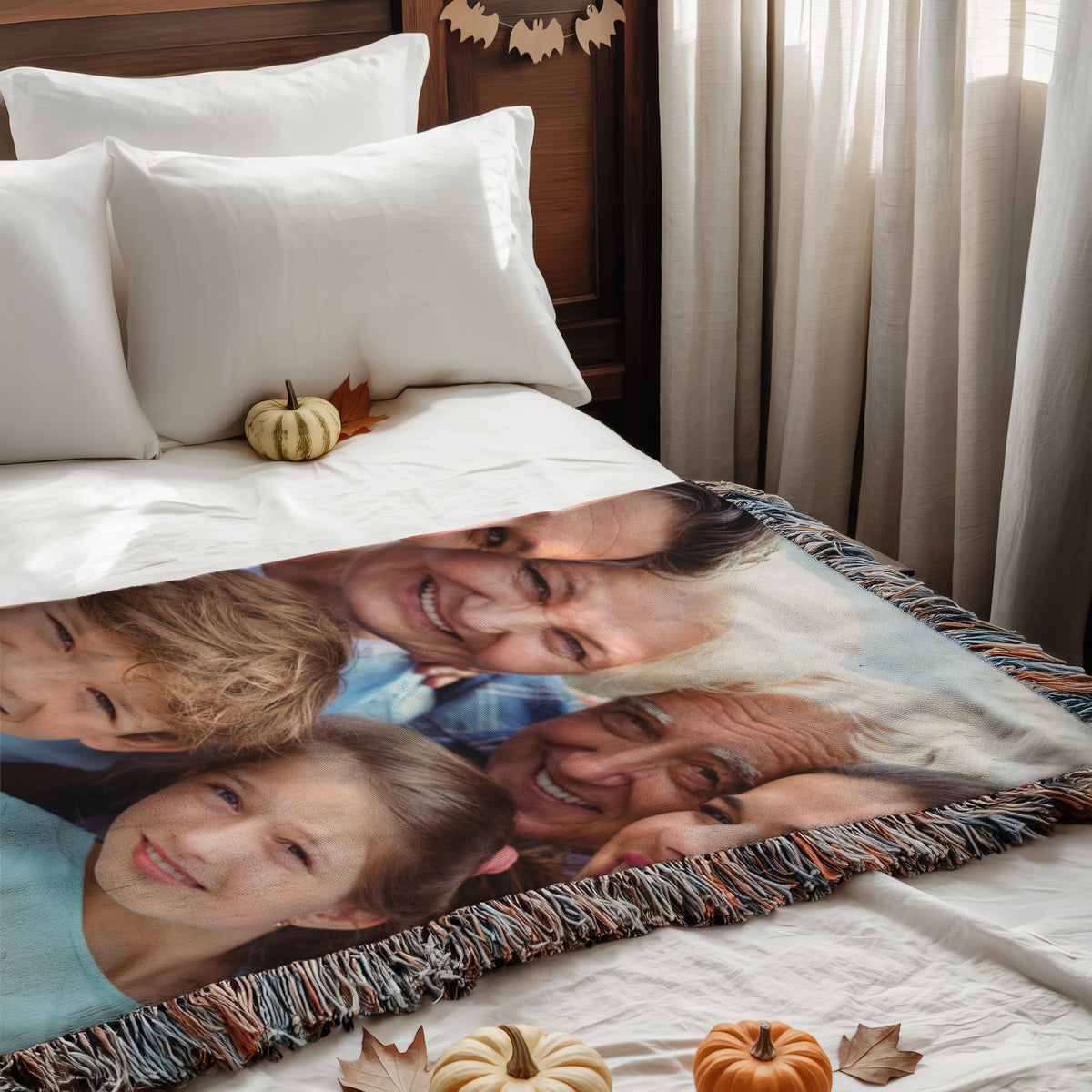 Queen size woven photo blanket of a family portrait spread across a bed with white bedding and small pumpkins
